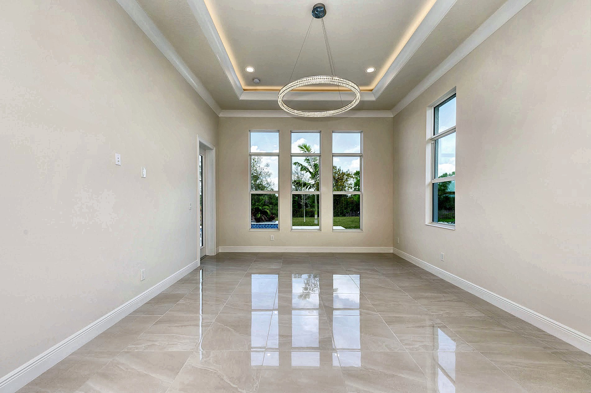 Empty room with a ring chandelier in a cove-lit tray ceiling and tall windows