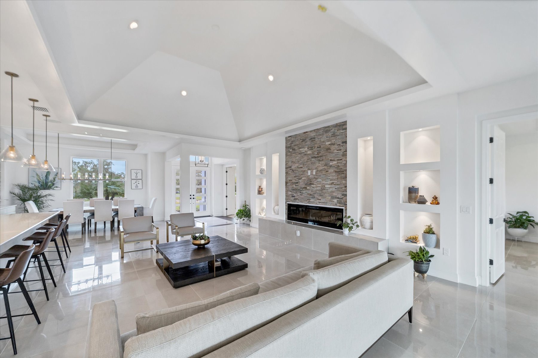 Bright great room with a stone fireplace, brass accent chairs and an open white kitchen