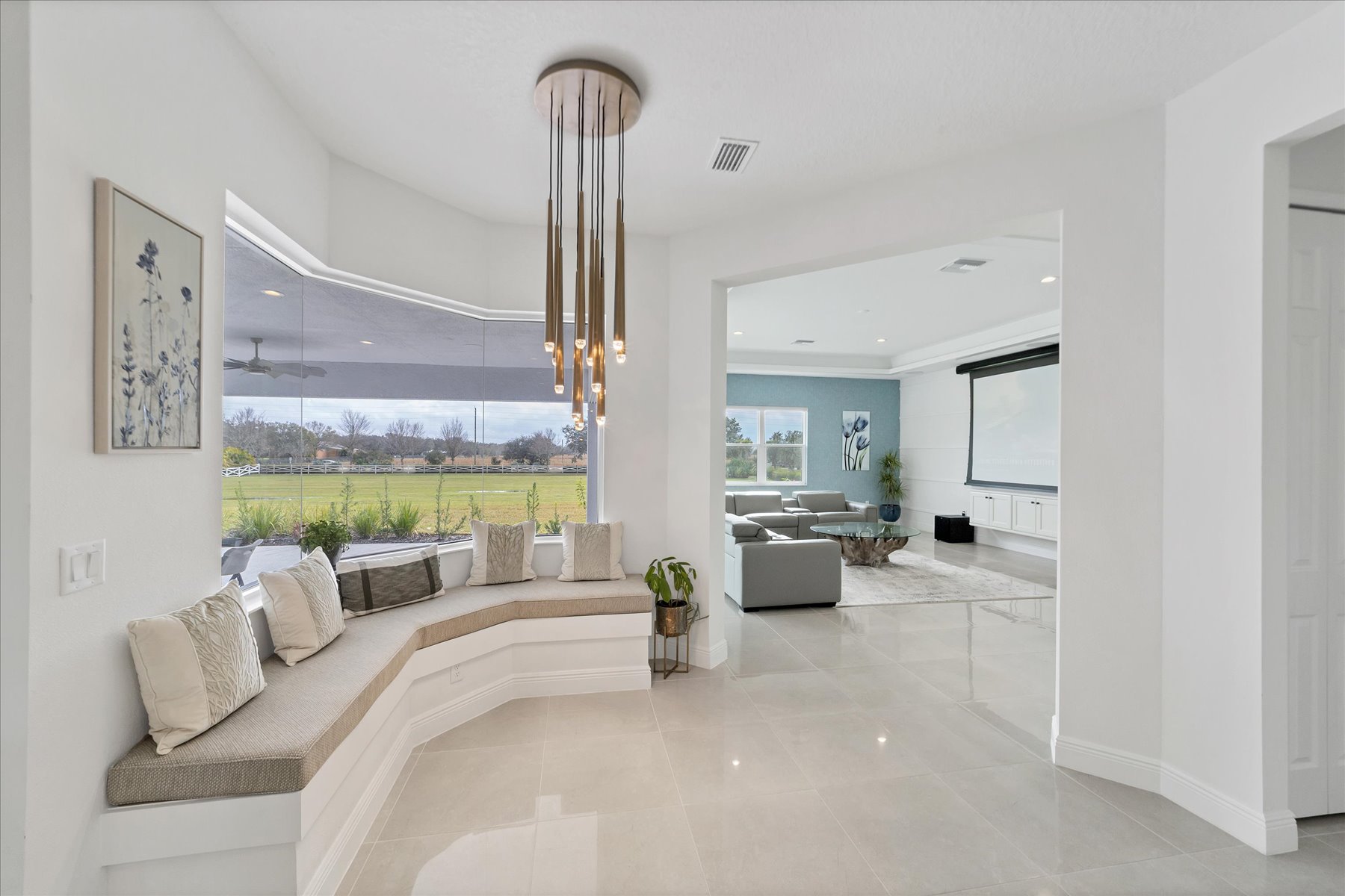 Light-filled living area with a neutral sofa, brass pendant and open views into the media room