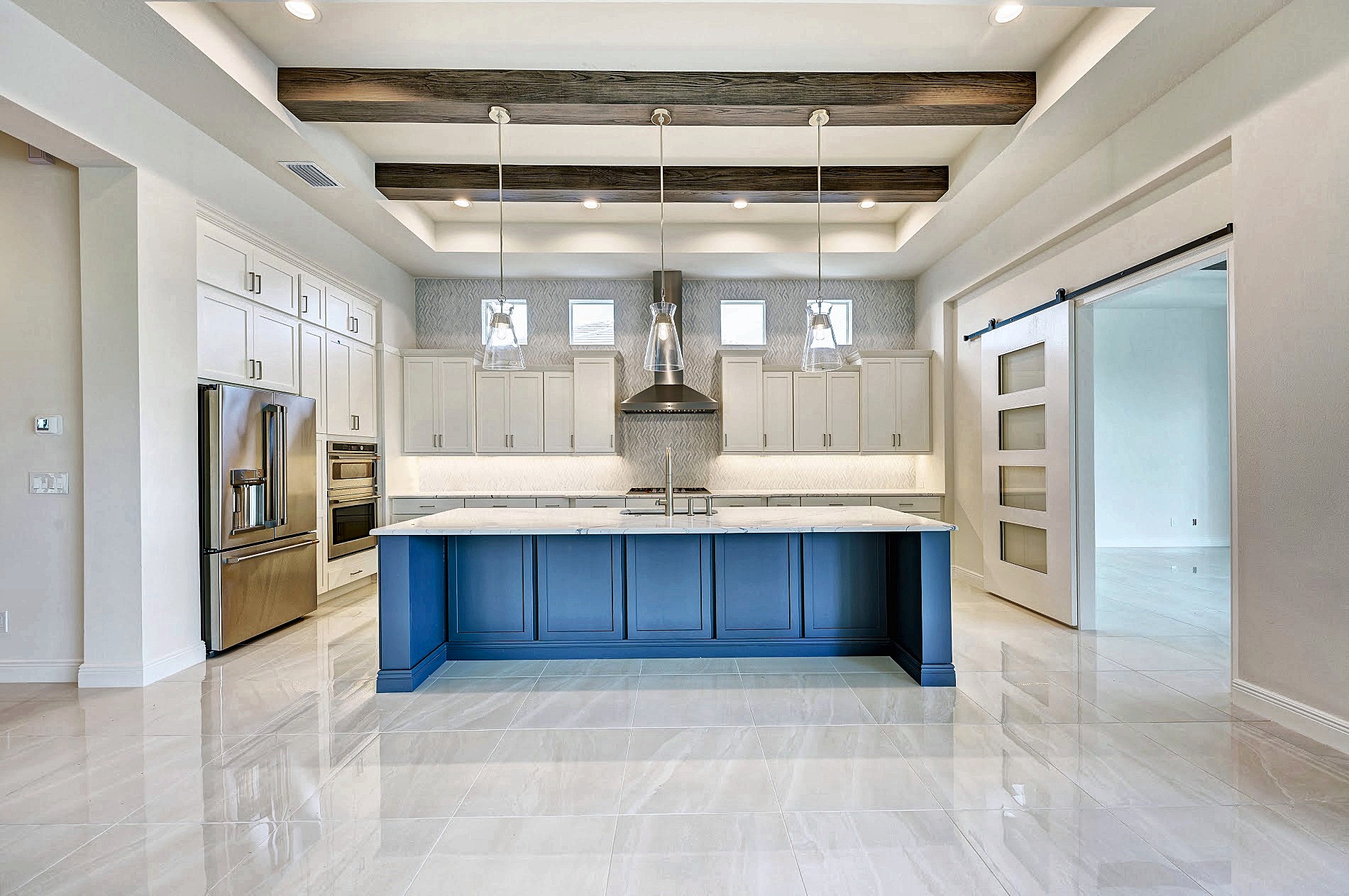Kitchen with white shaker cabinets, a navy island, wood-look ceiling beams and glass pendants