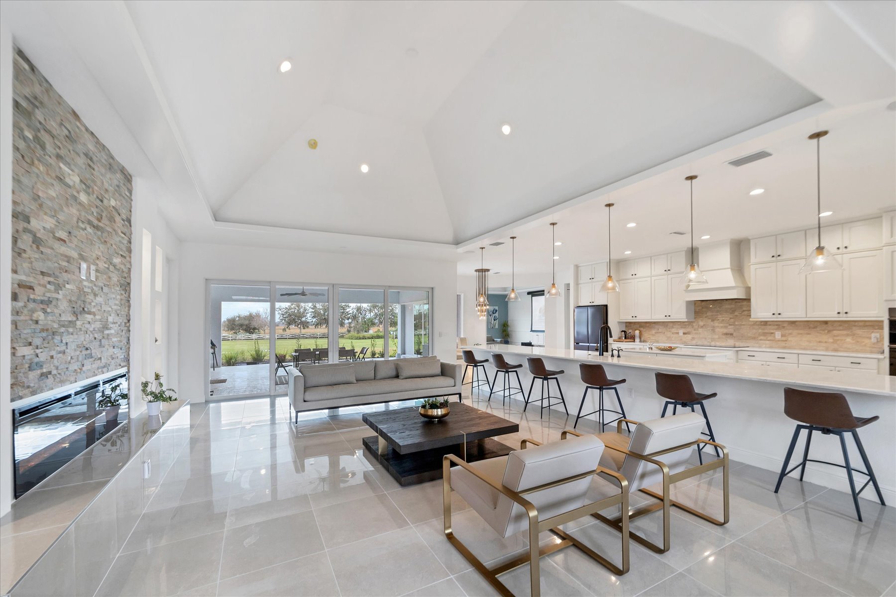 Great room with a neutral sofa, brass-framed accent chairs and an open view of the kitchen