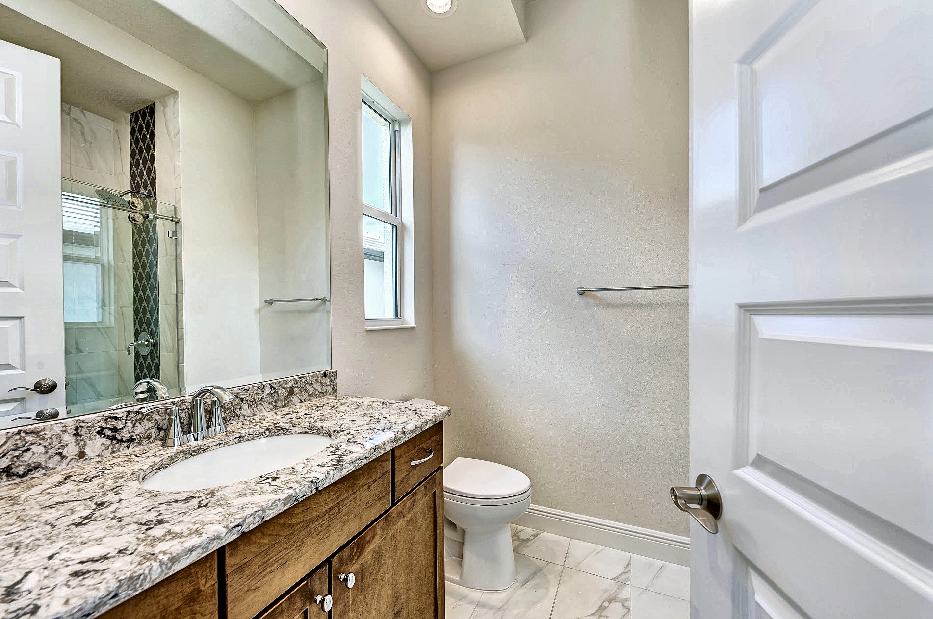 Guest bath with a warm wood vanity and veined stone counter