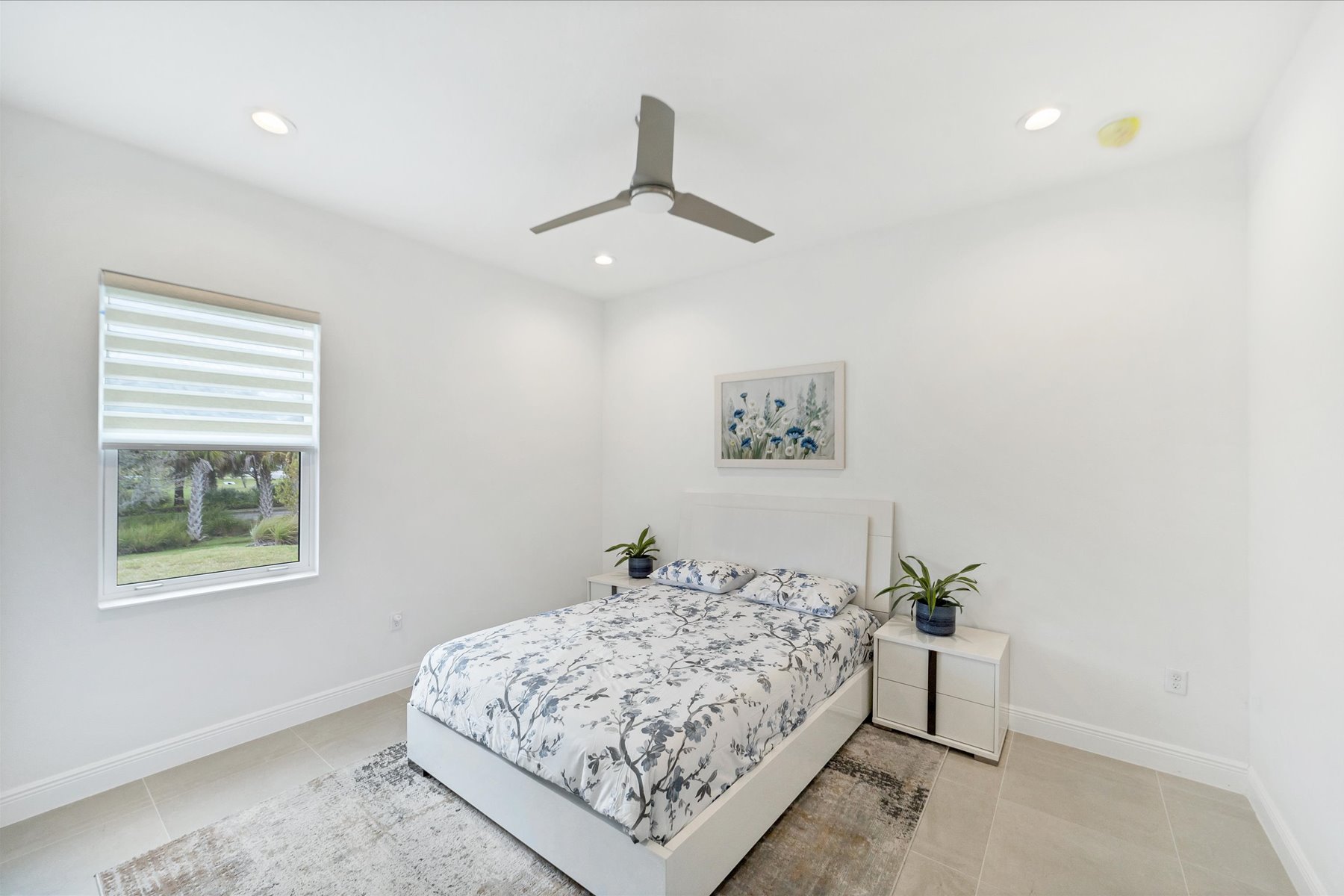 White guest bedroom with a blue floral quilt, matching plants and framed floral print